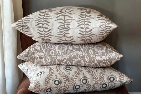 Three patterned pillows stacked on a brown surface against a gray wall.